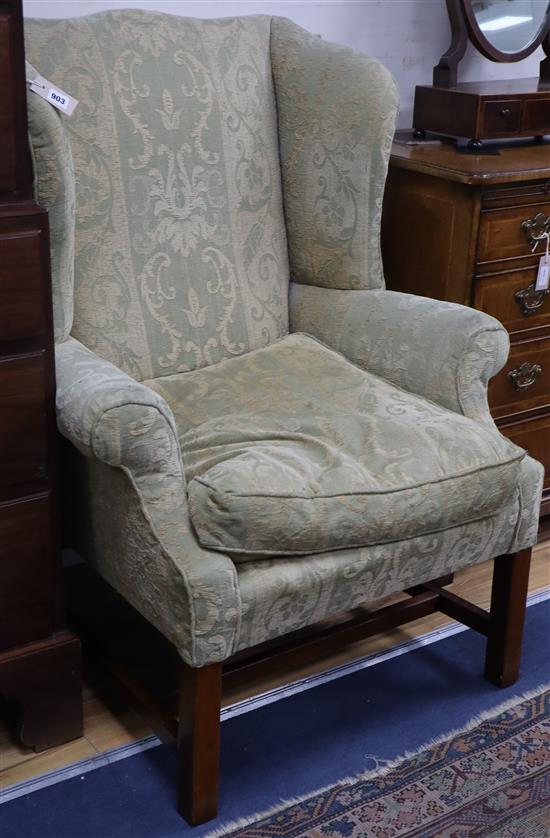 A Georgian style mahogany shaped wing armchair with green upholstery, square supports and H-stretcher